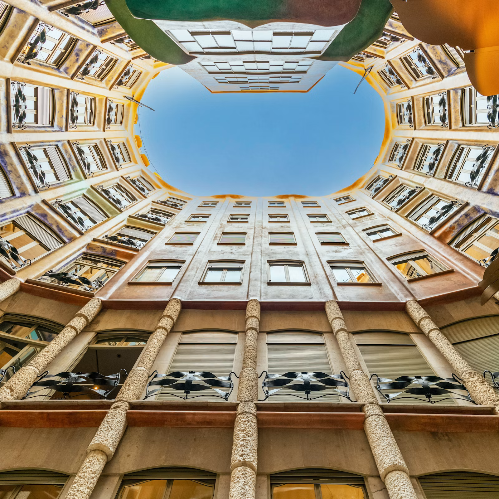 Patio interior de Casa Milà visto desde abajo, con ventanas onduladas y cielo azul